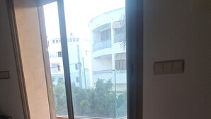 Une pièce dotée d’une grande porte-fenêtre coulissante qui donne sur un espace extérieur avec un sol carrelé et une vue sur un immeuble.