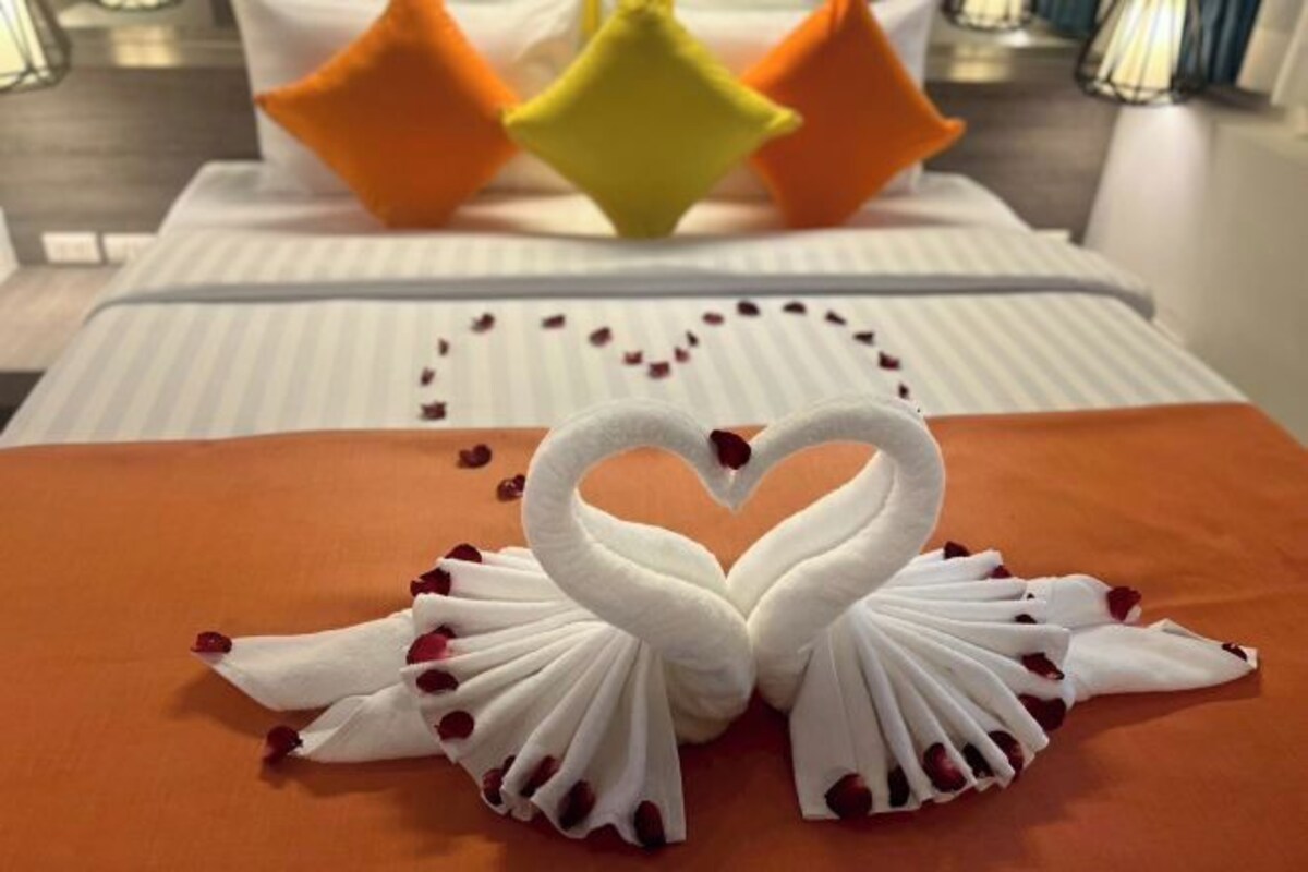 Una cama con una toalla dispuesta en forma de corazón y almohadones decorativos.