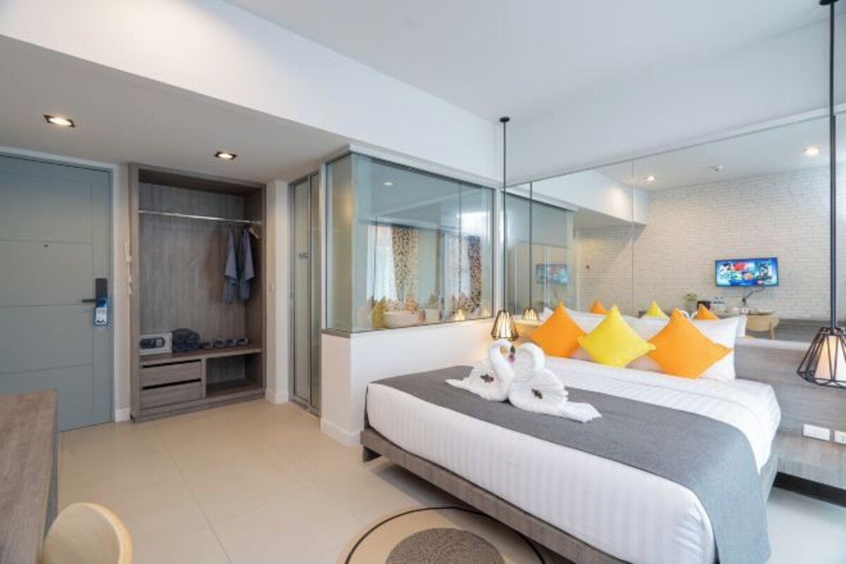 Habitación de hotel moderna con una cama grande, vestidor, separador de vidrio y televisor.
