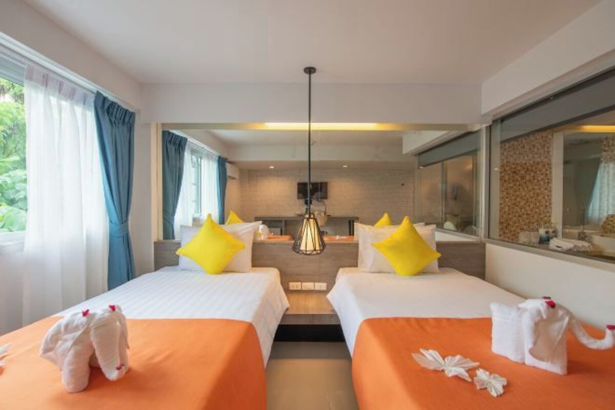 Habitación de hotel con dos camas, un kitchenette, un ventanal grande con cortinas y una lámpara colgante.