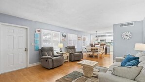 A living room with a gray sofa, two gray armchairs, a coffee table, and a dining area with a table and chairs. - Ilios Rentals (Fort Lauderdale)