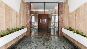 Un lobby moderno con suelo de mármol, paneles de madera y la entrada de un ascensor de cristal.