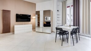 Una sala de estar moderna con televisor de pantalla plana, comedor con mesa y sillas, armario empotrado y un amplio ventanal con cortinas.