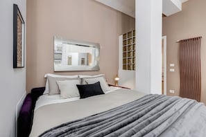 A modern bedroom with a bed, a mirror, a nightstand, and a window with blinds.