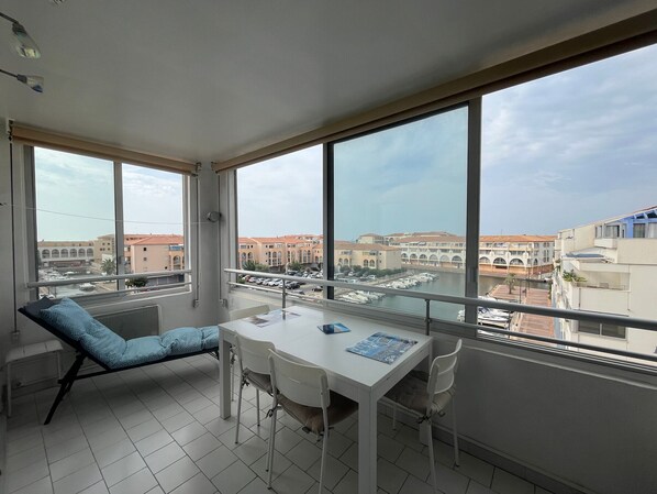 A balcony with a view of a marina and buildings. There is a table with chairs and a blue cushion.