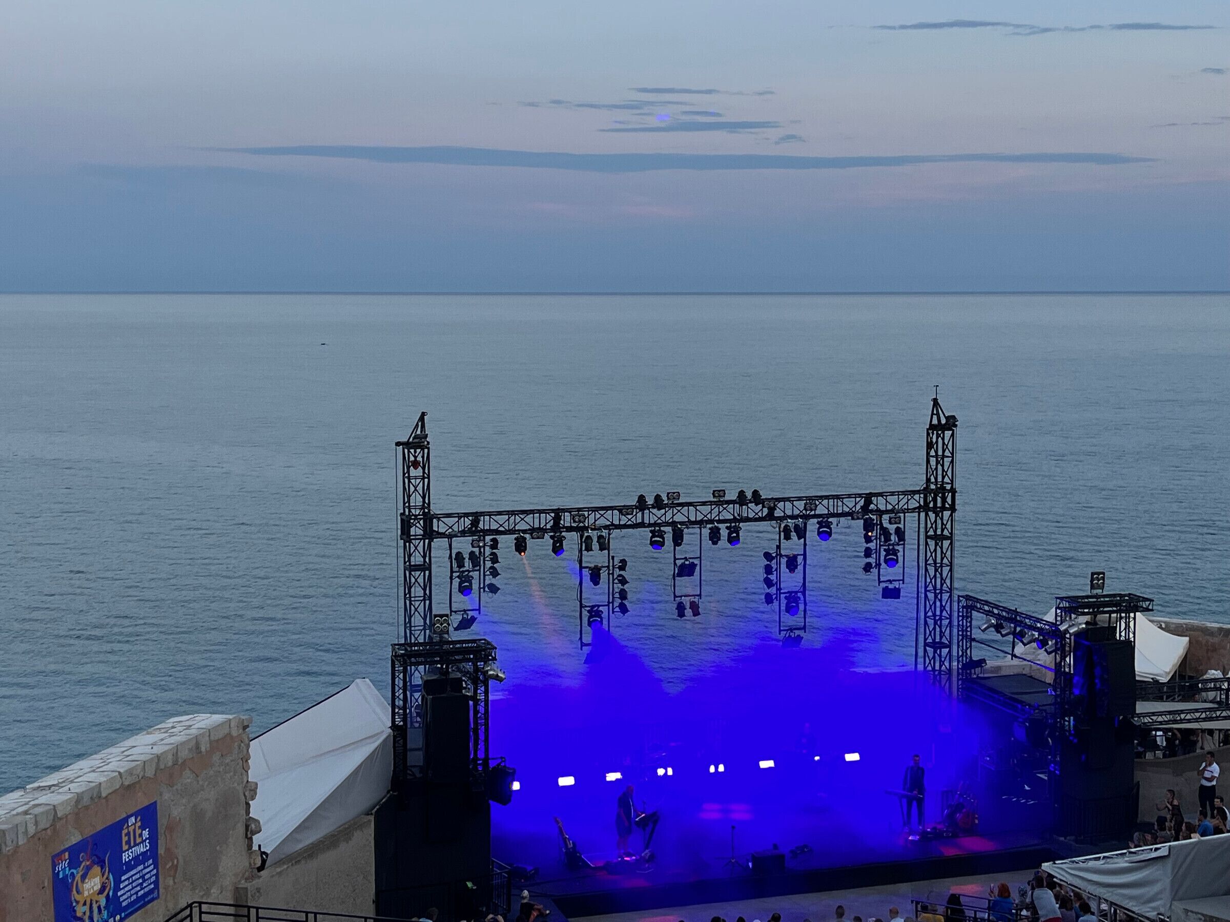 Een podium met een truss constructie en verlichting, met uitzicht op een wateroppervlak.