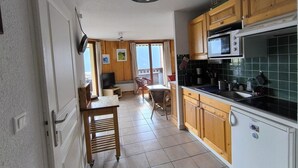 Een kleine keuken met houten kastjes, een magnetron en een eethoek met een tafel en stoelen.