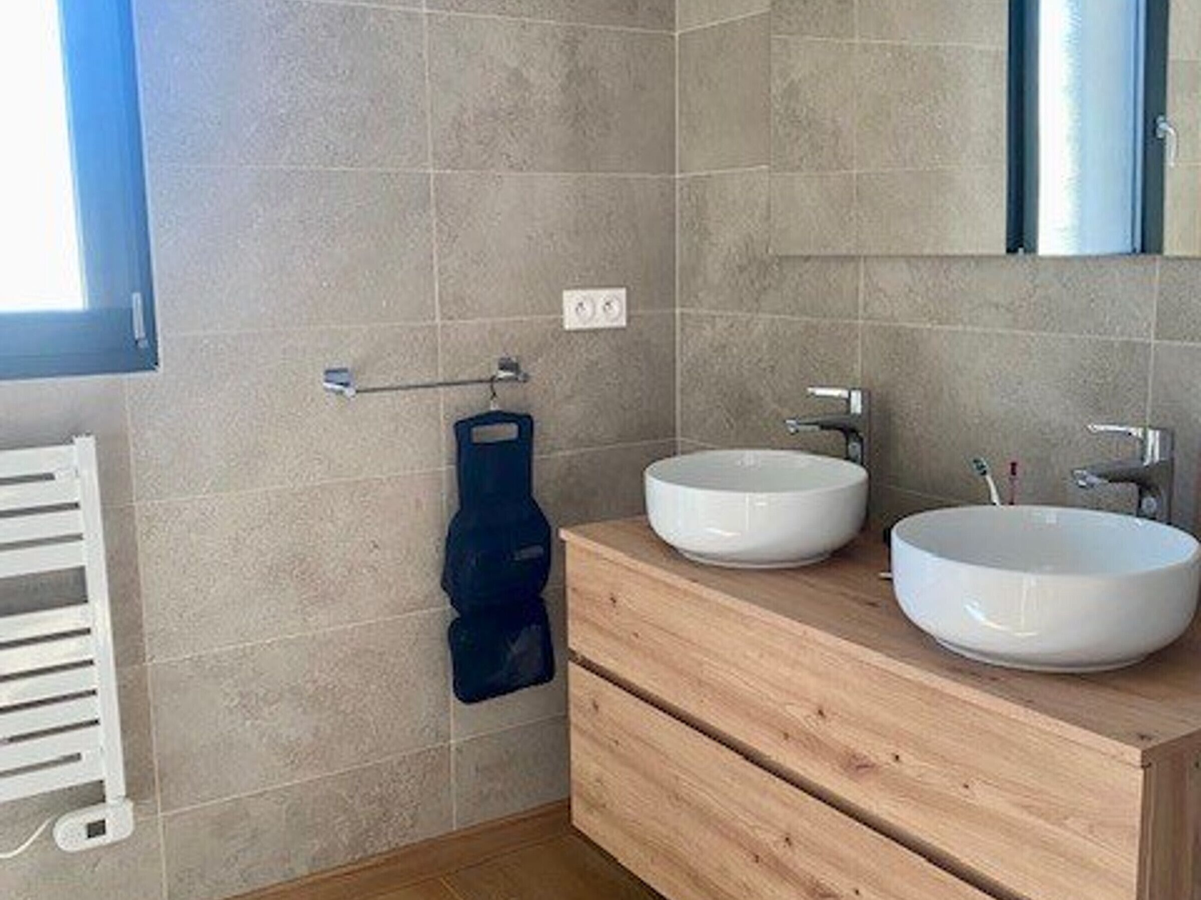 A modern bathroom with two white sinks, a wooden vanity, a towel rack, and a mirror.
