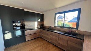 A modern kitchen with dark cabinets, a wooden countertop, and a window with a view of a house. - Luxury chalet for 10 with parking in Font Romeu (Font-Romeu-Odeillo-Via)