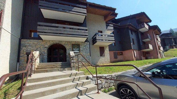 A building with a stone facade, a wooden staircase, and a car parked in front.