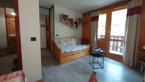 A cozy room with a wooden sofa, a small table, and a window with curtains.