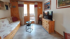 A cozy room with a wooden bed, a small table, a TV on a wooden cabinet, and a painting on the wall.
