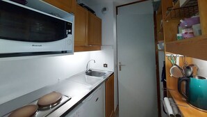 A compact kitchen with a Brandt microwave, a sink, and wooden cabinets.