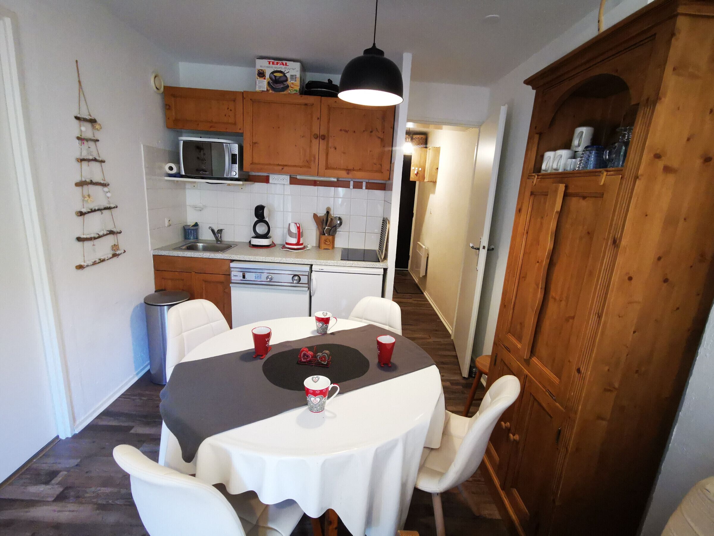 A compact kitchen with wooden cabinets, a microwave, and a sink. There is a dining table with chairs and a few cups.