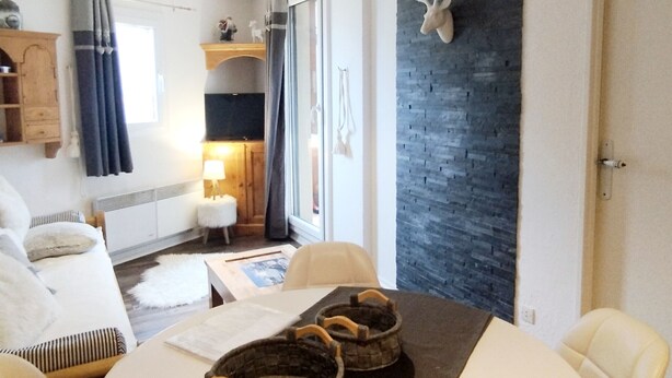 Ein modernes Wohnzimmer mit Esstisch, Stühlen, Kamin und einer Steinwand, an der ein Reh aufgehängt ist.