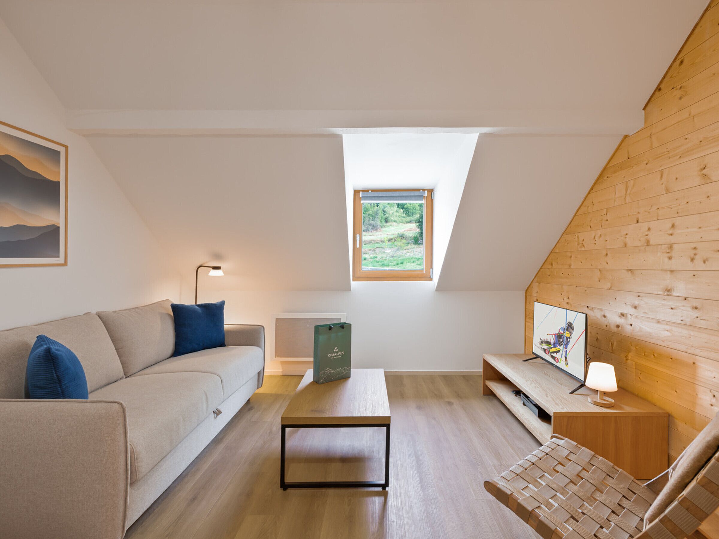 A modern loft bedroom with a sloped ceiling, a wooden desk, a sofa, a small table, and a bed.