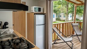 A compact kitchen with a gas stove, a microwave, and a refrigerator. There is a wooden deck with a chair and a view of a residential area. - Cozy mobile home for 4 with terrace (Granges-Aumontzey-Aumontzey)