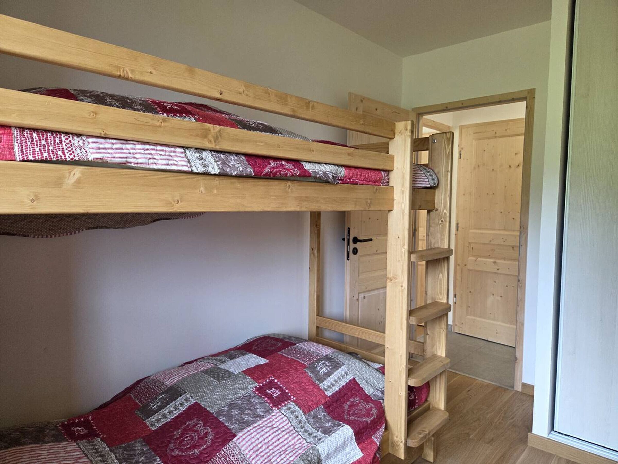 A bunk bed with a patterned quilt, a wooden door, and a small shelf unit.