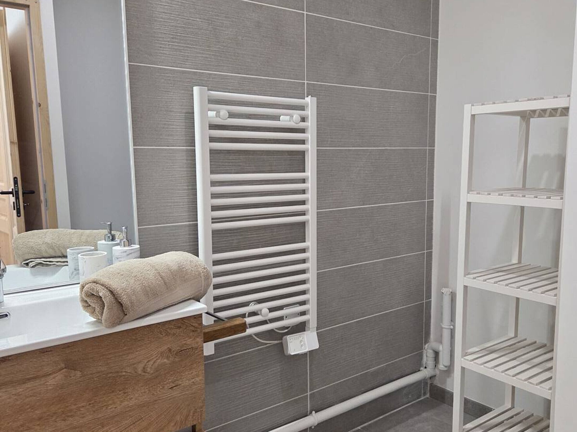 A bathroom with a white towel rack, a mirror, a sink, and a white shelving unit.