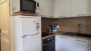 A compact kitchen with a refrigerator, microwave, coffee maker, and oven. - New 3-room apartment with parking and balcony in Valmorel (Valmorel)