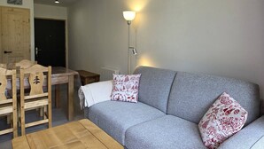 A cozy living room with a grey sofa, two patterned pillows, a wooden coffee table, a floor lamp, and a dining area with a wooden table and chairs. - New 3-room apartment with parking and balcony in Valmorel (Valmorel)