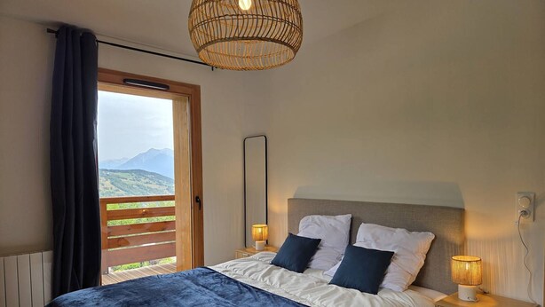 A bedroom with a large bed, two bedside lamps, a mirror, and a view of the outdoors. - Charming T2 Valmorel, balcony, covered parking (Valmorel)