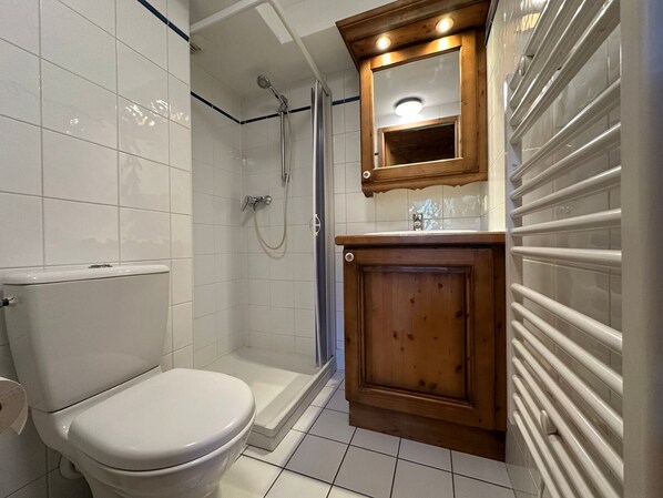 A bathroom with a toilet, shower, and wooden cabinet.