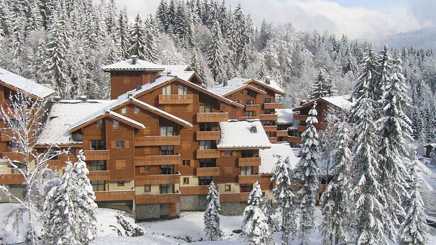 Un chalet en bois à plusieurs étages, doté de balcons et entouré d’arbres couverts de neige.