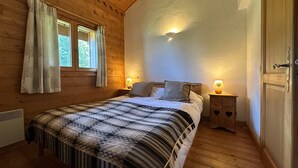 Une chambre confortable, aménagée dans un chalet en bois, avec un grand lit, deux lampes de chevet et une fenêtre avec des rideaux.