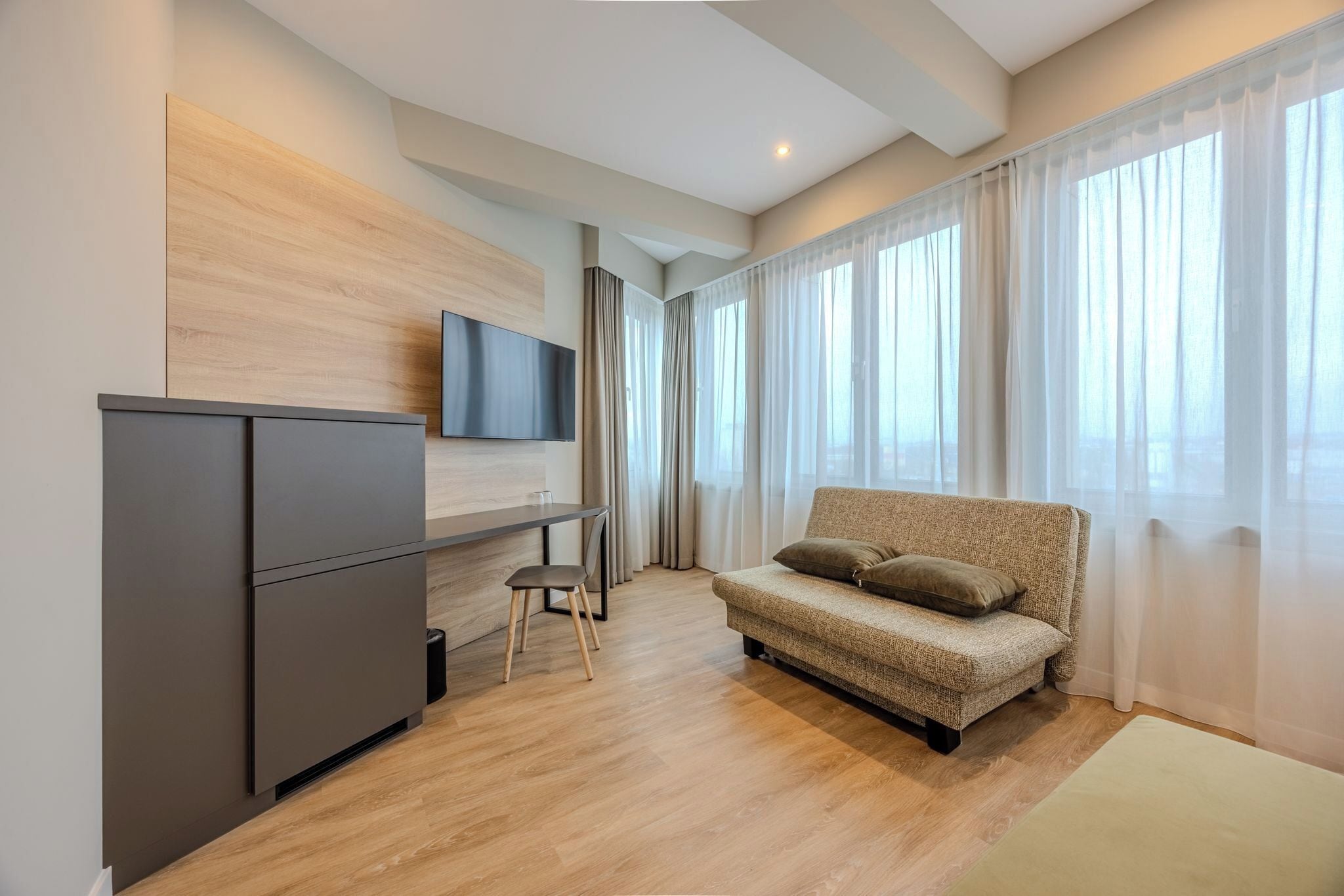 A modern living room with a sofa, a flat-screen TV mounted on the wall, a small table, and a cabinet.