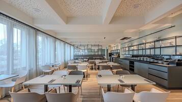 A modern dining area with tables and chairs, a kitchen area with shelves, and large windows with curtains.