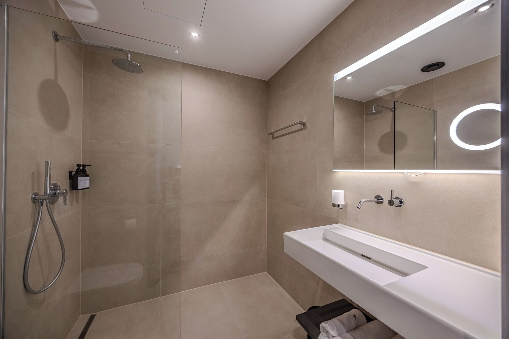 Un baño moderno con cabina de ducha de vidrio, un lavabo blanco y un espejo con iluminación integrada.