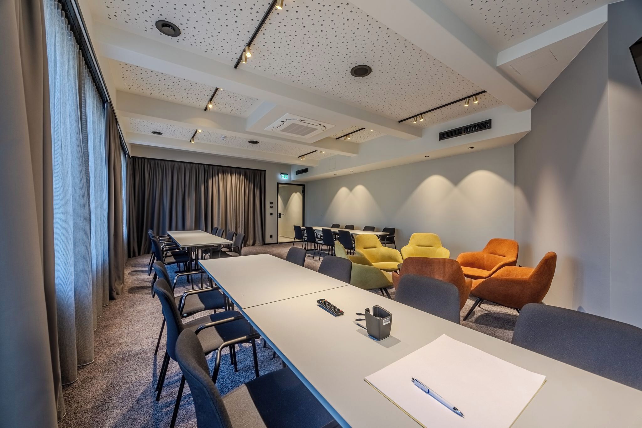 Ein moderner Konferenzraum mit einem langen Tisch, mehreren Stühlen und vielfältigen Sitzgelegenheiten in unterschiedlichen Farben.
