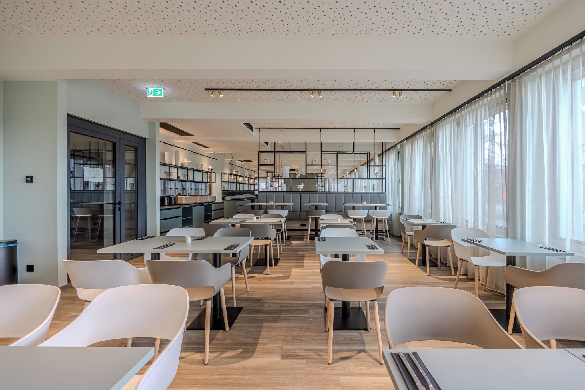 A modern dining area with tables and chairs, a staircase, and a view of the city through large windows.