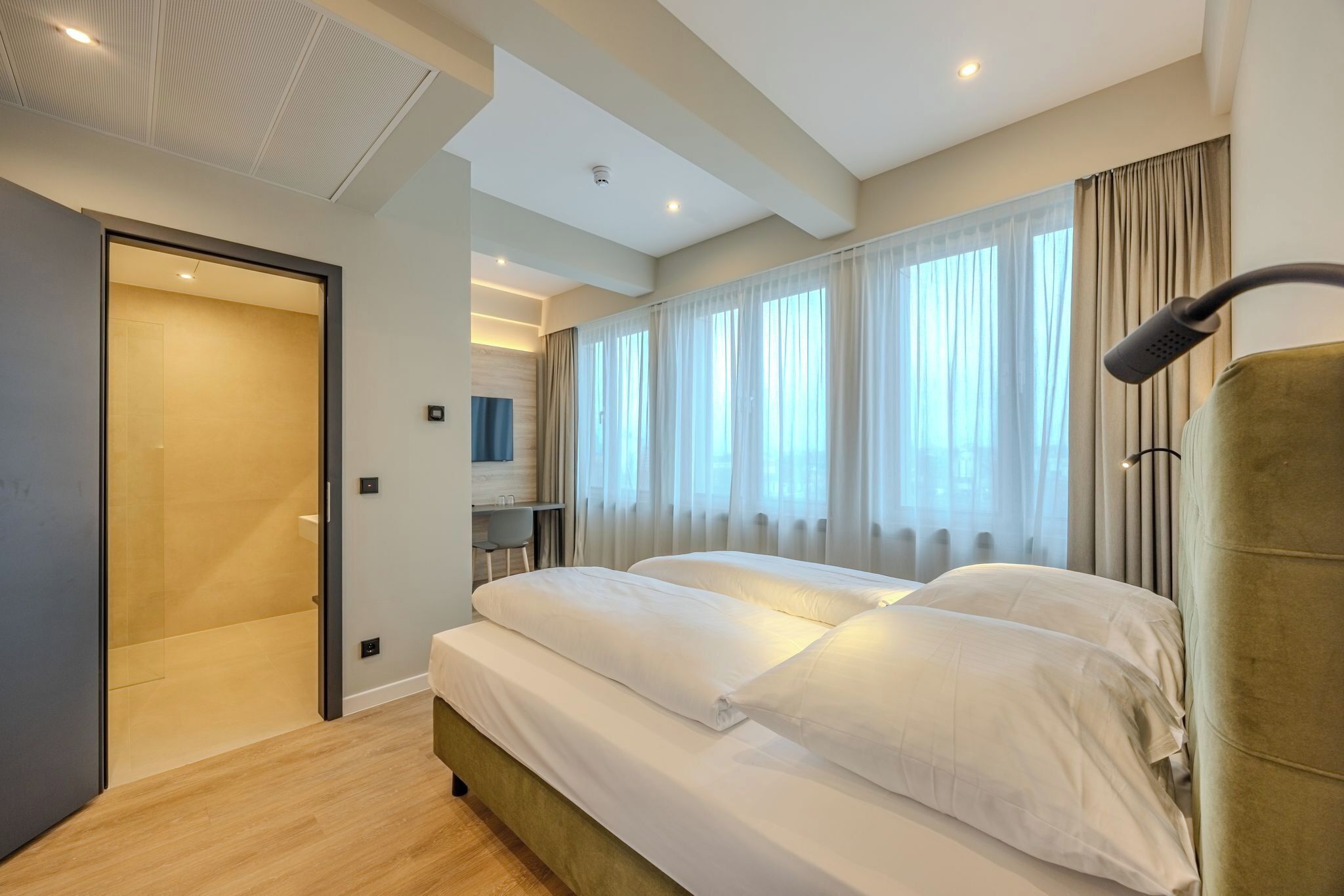 A modern hotel room with a large bed, a desk, and a shower area.