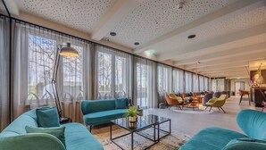 Un hall d’hôtel spacieux, avec des canapés de couleur turquoise, une table basse en verre et un lustre moderne.
