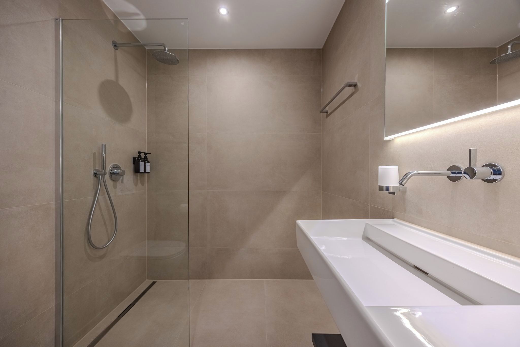 A modern bathroom with a glass-enclosed shower, a white sink, and a mirror with integrated lighting.