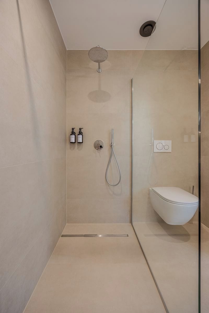 Un espace douche moderne doté d’une paroi en verre, d’un pommeau de douche à main et de toilettes.