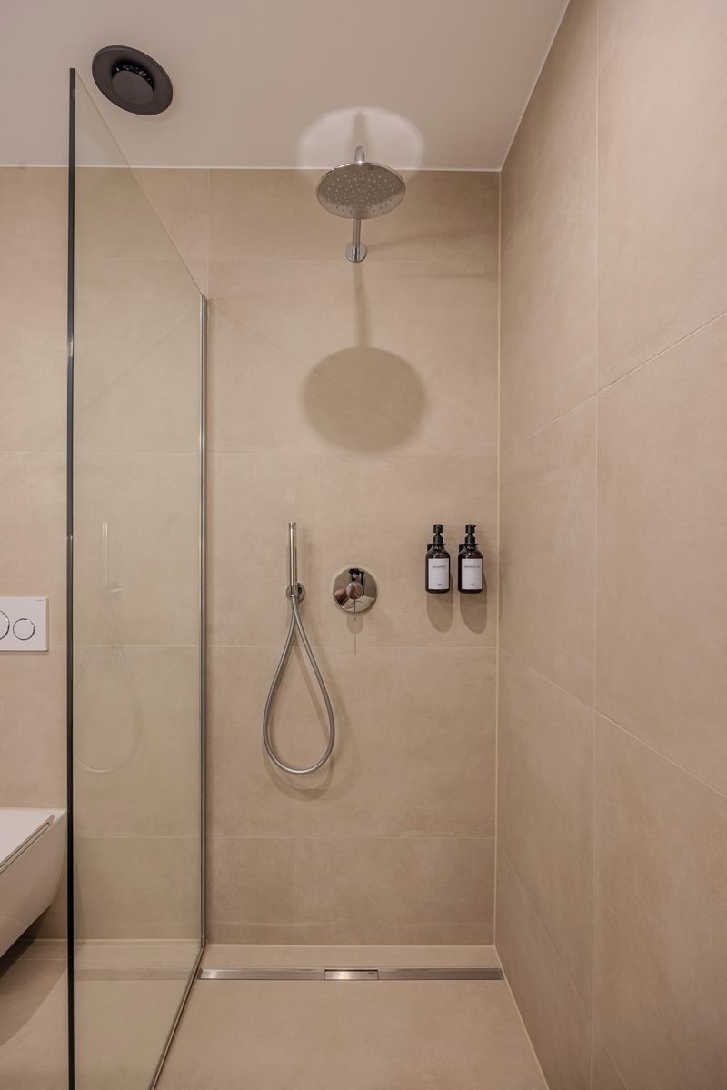 Un área de ducha moderna con mampara de vidrio, un cabezal de ducha manual y dos botellas de champú.
