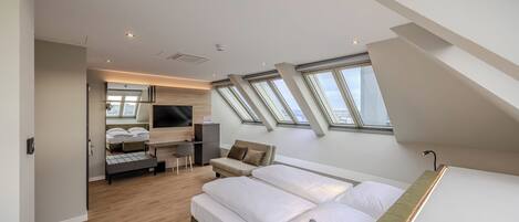 A modern hotel room with a lofted ceiling, skylights, a bed, a seating area, and a TV.