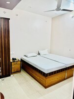 Ein Schlafzimmer mit einem hölzernen Bettgestell, zwei weißen Matratzen, einer kleinen Holzkommode und einem Deckenventilator.