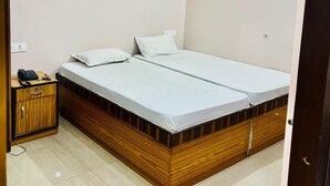 Una cama individual con estructura de madera y ropa de cama blanca, una mesita de noche pequeña con un teléfono y un ventilador de techo.