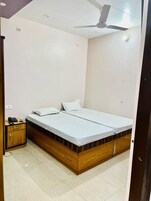 Ein Einzelbett mit Holzrahmen und weißer Bettwäsche, ein kleiner Nachttisch mit Telefon sowie ein Deckenventilator.