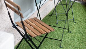 A patio area with two wooden tables and two chairs, set on artificial grass, next to a building with a window. - Route 99 Yumoto (Hakone)
