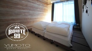A modern guest room with a wooden wall, a bed with white bedding, a hanging light fixture, and a window with curtains. - Route 99 Yumoto (Hakone)