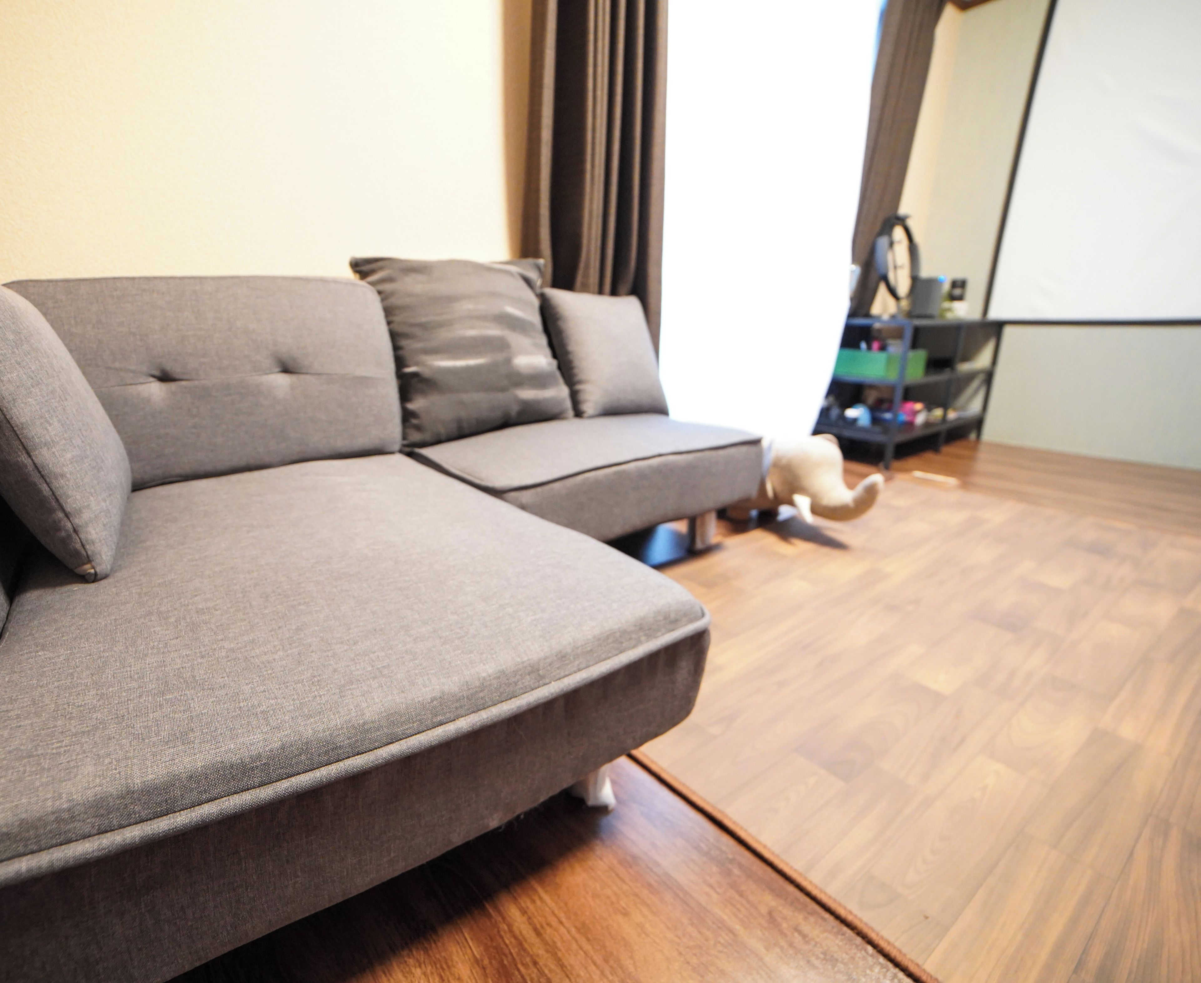 A grey sectional sofa with a wooden floor and a black shelf in the background.
