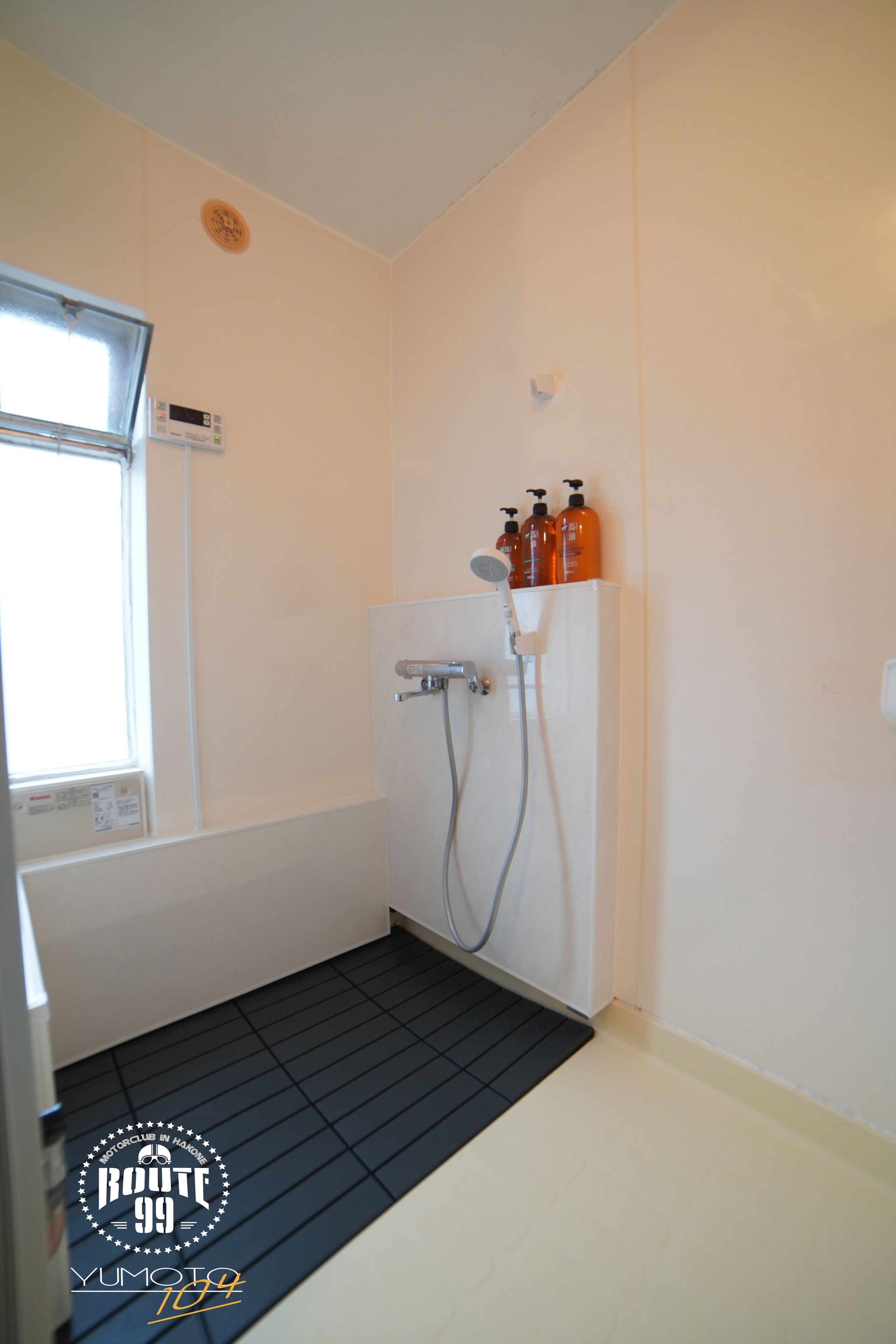 A bathroom with a shower, a window, and a thermostat on the wall.