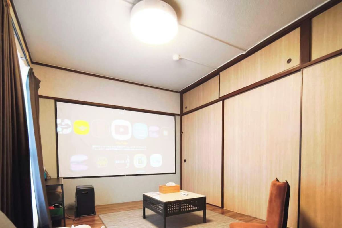 A room with a projector screen displaying icons, a speaker, a small table, and a chair.