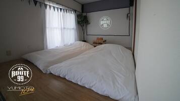 Een kamer met twee bedden, een raam met dunne gordijnen, een wandprojectiescherm en een houten vloer.