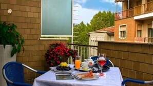 Un balcon avec une table préparée pour le petit-déjeuner, comprenant une assiette de nourriture, un verre de jus et une théière.